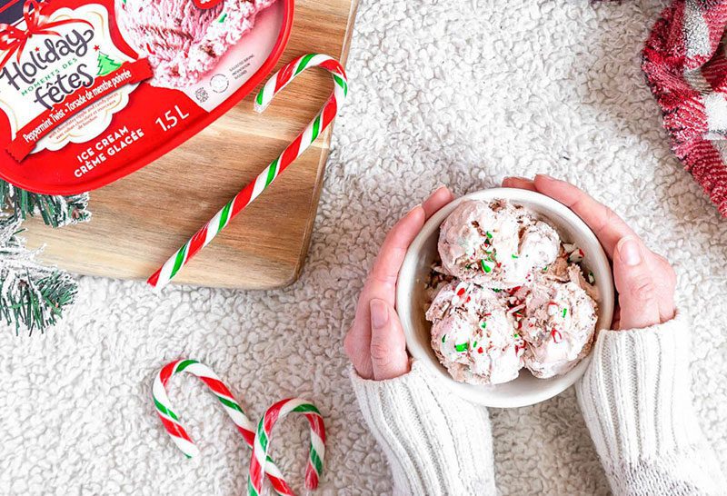 A woman's hands holding a bowl of Chapman's Peppermint Twist Ice Cream with candy canes on a marble counter top