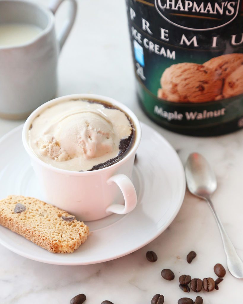 a scoop of Chapman's Maple Walnut ice cream in a white coffee mug on a white saucer with coffee beans scattered around the table underneath