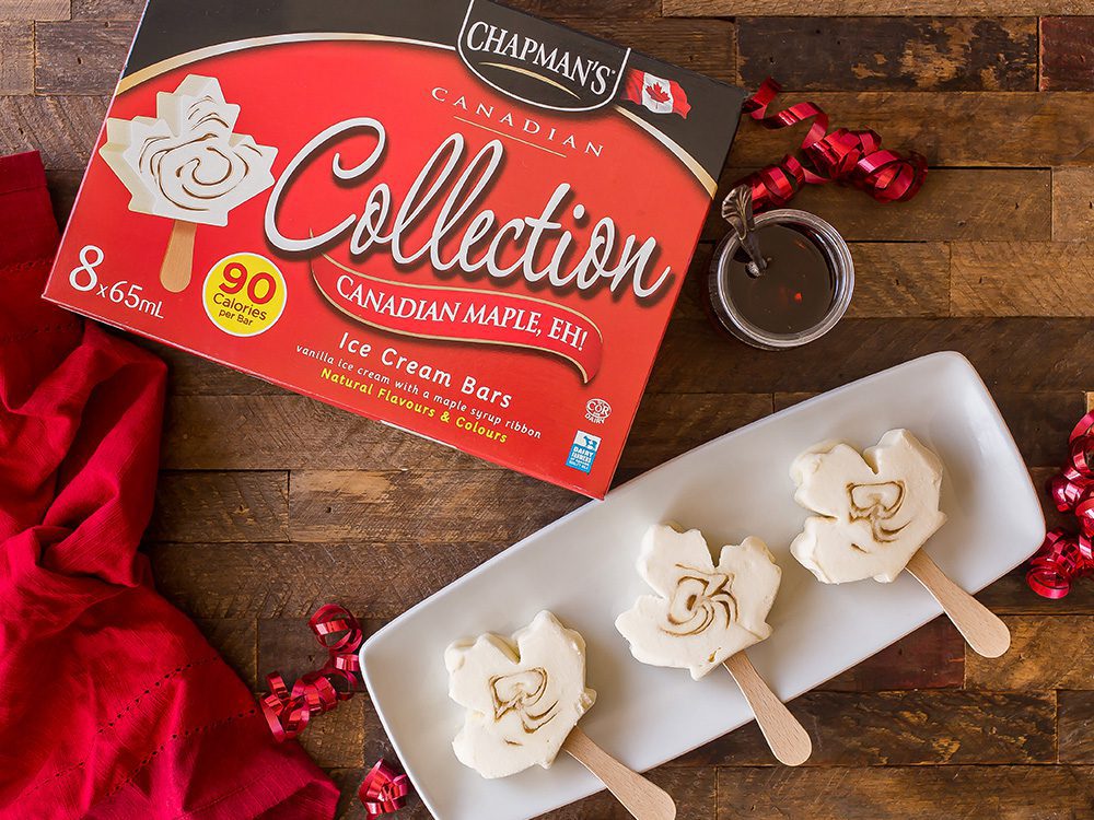 Trois barres de crème glacée érable Canadien, hé! posées côte à côte sur une assiette rectangulaire blanche sur une table en bois avec un petit plat de sirop d’érable