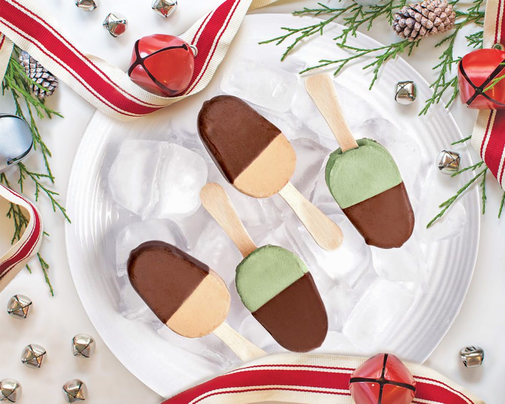 Four of Chapman's Holiday Moments ice cream bars placed on top of ice on a white dinner plate with Christmas ribbon, jingle bells, and a pine branch around the plate for Christmas decor