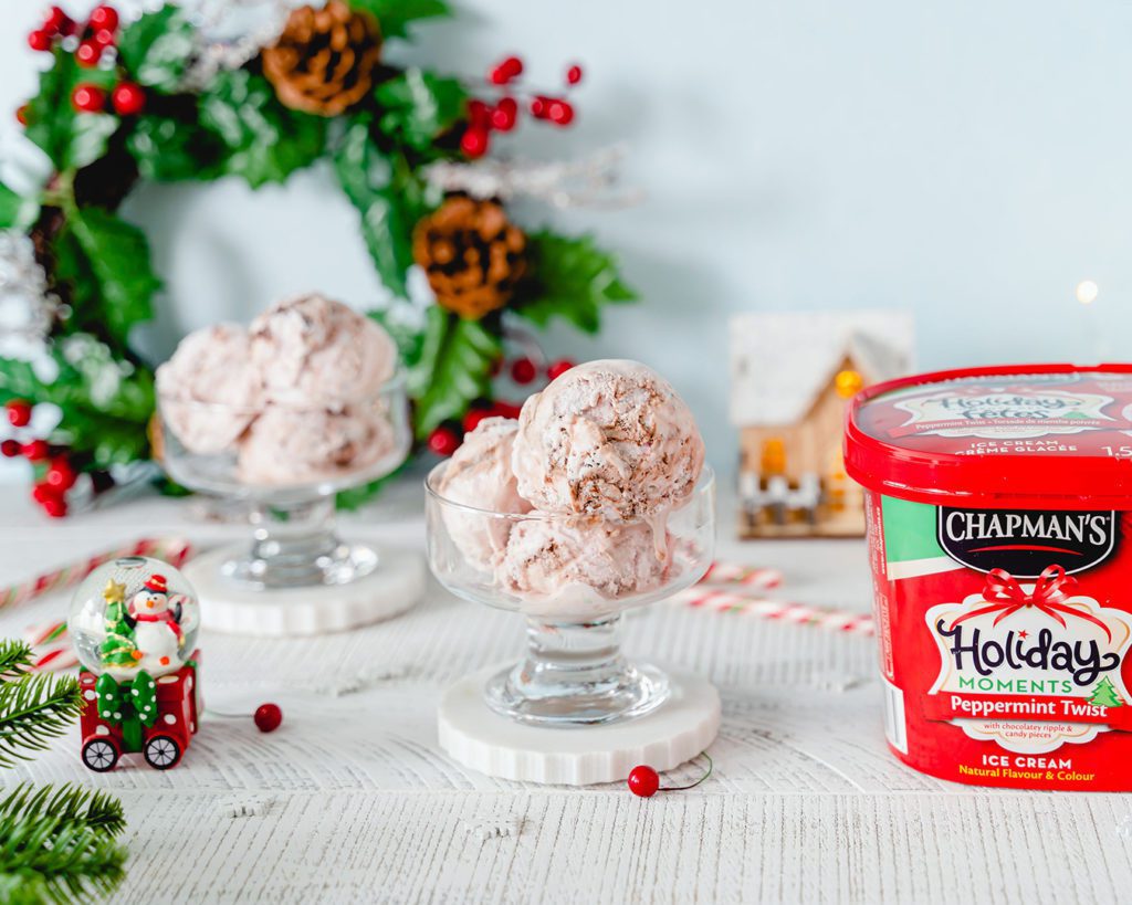 A glass bowl filled with three scoops of Chapman's Peppermint Twist ice cream beside the 2L tub and a small snowglobe with a festive penguin inside