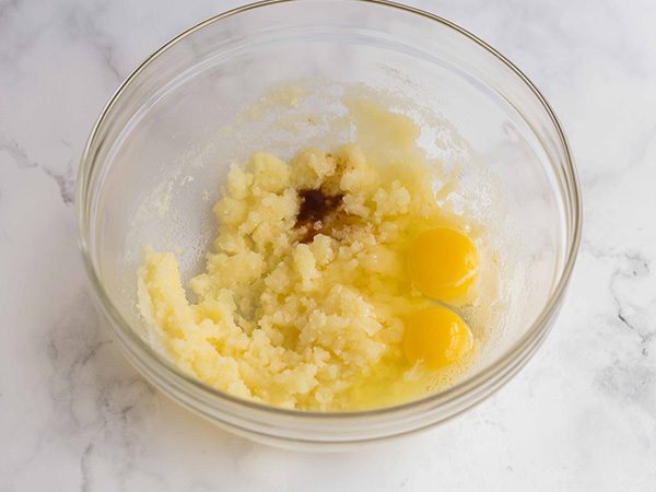 glass mixing bowl with sugar and butter mixture, plus eggs and vanilla