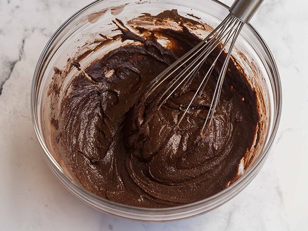 whisk inside a glass mixing bowl with mixed brownie batter