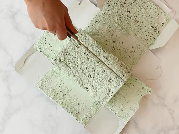 person's hand cutting a slice of Chapman's Mint Chip ice cream from an open carton