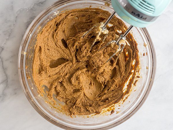 hand mixer on the side of a glass bowl with whipped butter, sugar, molasses and eggs