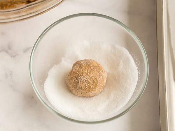 cookie dough rolled in ball and white sugar sitting in small glass bowl of white sugar
