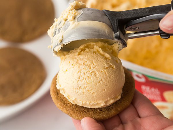 close up of person's hand scooping Shortbread ice cream onto a cookie with an ice cream scooper