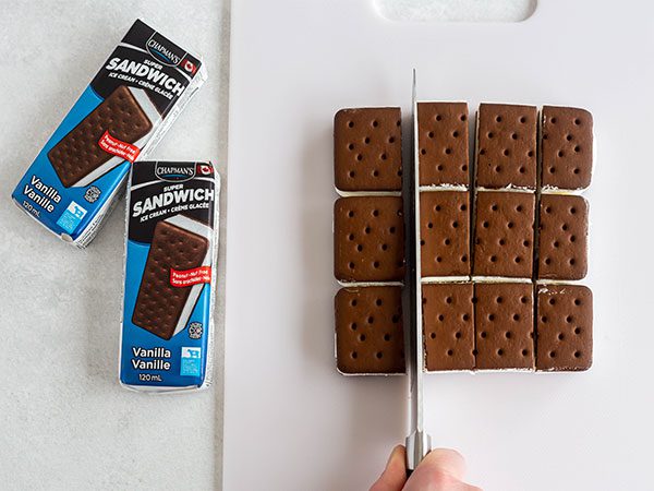 On a white counter, three Chapman's vanilla ice cream sandwiches laid side by side being cut into four equal pieces