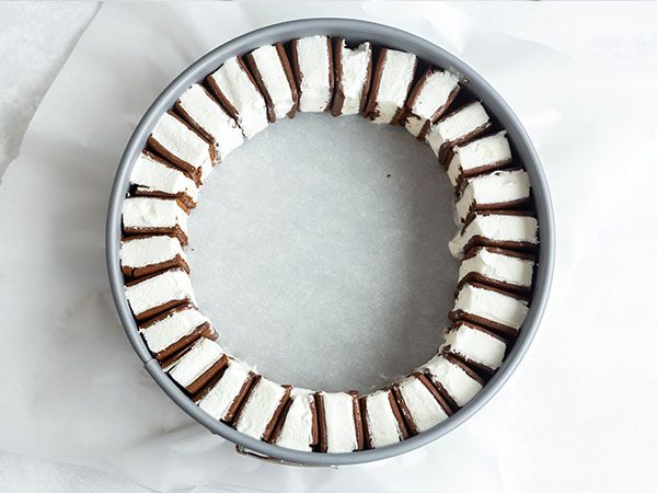 A springform pan lined with parchment paper with a ring of sliced ice cream sandwiches along the inside border