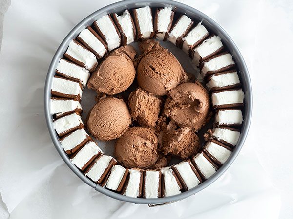 A springform pan lined with parchment paper with a ring of sliced ice cream sandwiches along the inside border with scoops of chocolate ice cream inside