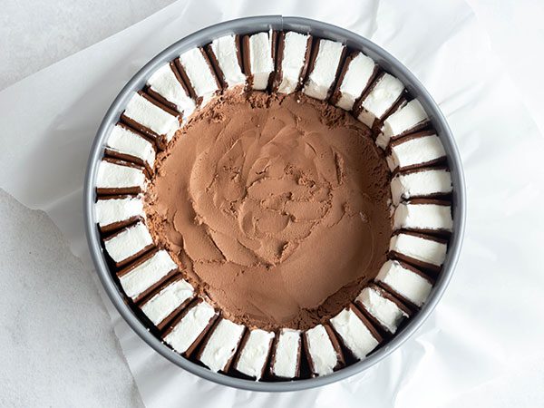 A springform pan lined with parchment paper with a ring of sliced ice cream sandwiches along the inside border with a layer of chocolate ice cream inside