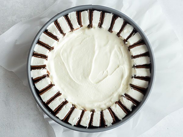 A springform pan lined with parchment paper with a ring of sliced ice cream sandwiches along the inside border with a layer of vanilla ice cream inside