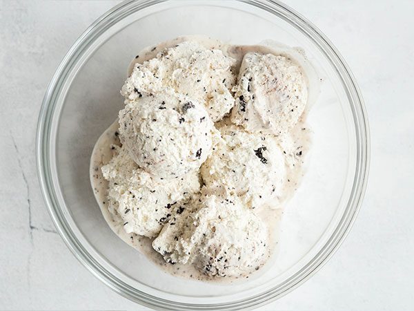 Scoops of cookies and cream ice cream slightly melted inside a clear mixing bowl