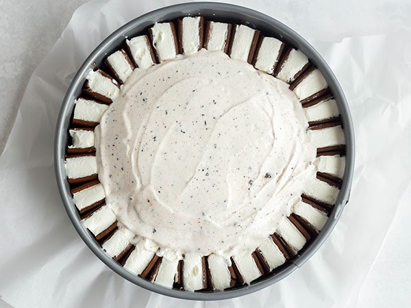 A springform pan lined with parchment paper with a ring of sliced ice cream sandwiches along the inside border with a layer of cookies and cream ice cream inside