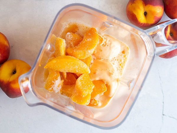 Looking from above into a blender with frozen peach slices and peaches and cream frozen yogurt