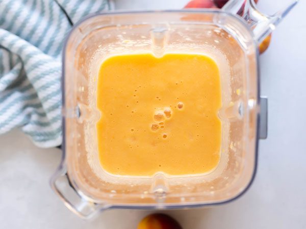 Looking from above into a blender with a rich orange coloured Peach Bellini Mocktail