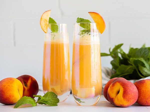 Two tall glasses filled with Peach Bellini Mocktail, garnished with a mint leaf and fresh peach slice