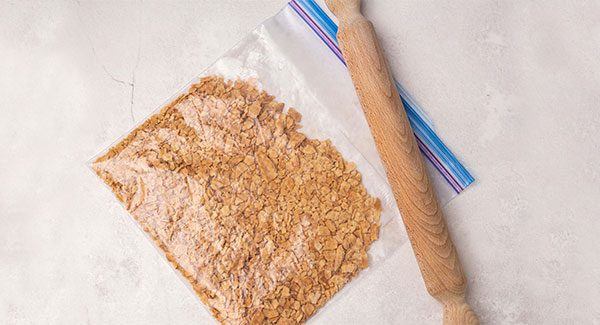 A closed zip top bag filled with crushed sugar cones. A rolling pin sits beside the bag.