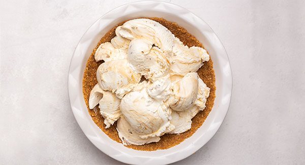 A white pie plate filled with a sugar cone crust and large scoops of Caramel Praline ice cream.