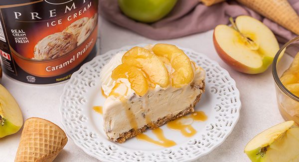 A slice of Caramel Apple Ice Cream Pie on a white decorative plate with a drizzle of caramel sauce on top.