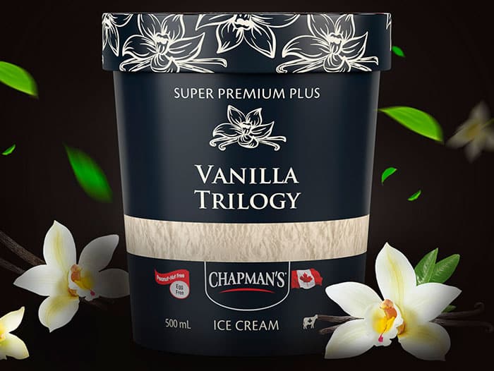 A tub of Chapman's Super Premium Plus Vanilla Trilogy ice cream on a black background with vanilla bean flowers beside.