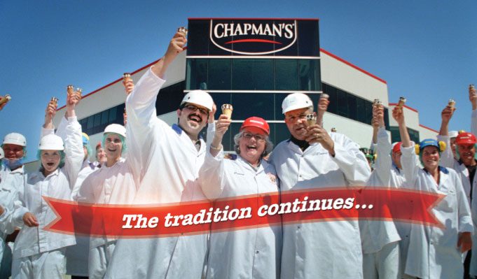 Standing in front of Chapman's Phoenix building in Markdale, Ontario, are a group of Chapman's employees along with Ashley, Penny, and David Chapman. They're all holding an ice cream up in the air while smiling. Text is overl