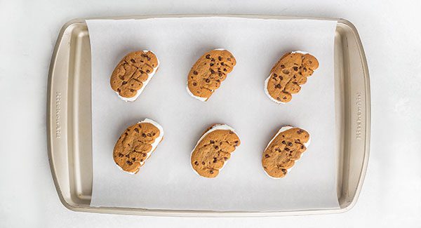 View from above of a group of six Chocolate Chip Ice Cream Sandwiches on a piece of parchment paper placed on a cookie sheet.