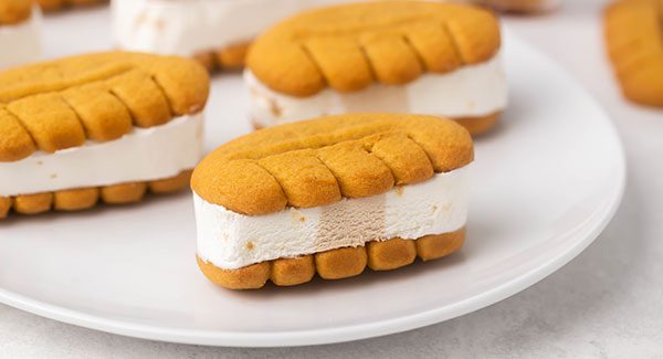 On a white plate are a few Maple Crunch Ice Cream Sandwiches. You can see a close up of the ice cream between two Bear Paws cookies.