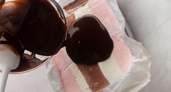 Melted Chocolate from a silver bowl is being poured onto our cake