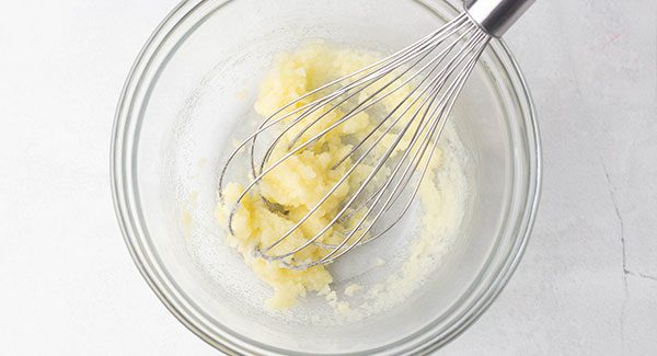 A glass bowl with butter and sugar being whisked