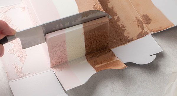 A knife is cutting thin slices of Neapolitan Ice Cream